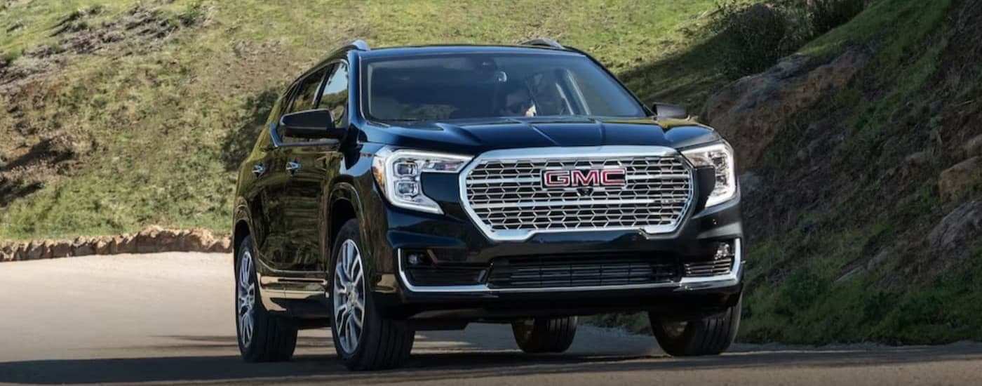 A black 2024 GMC Terrain driving on a backroad.
