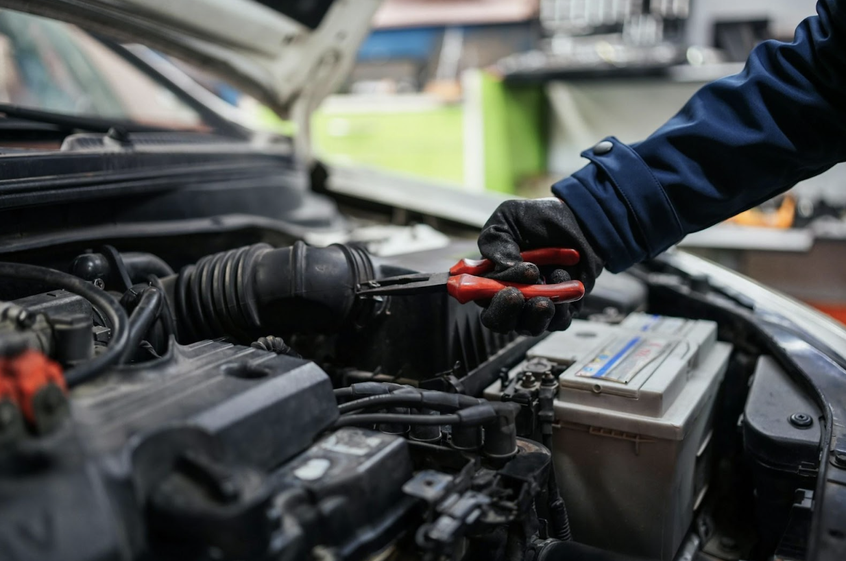 Close-up of a mechanic in gloves using pliers to work on a car engine under the hood.