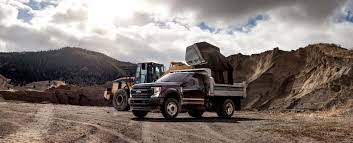 a dark blue ford in a canyon taking dirt from a front end dumper