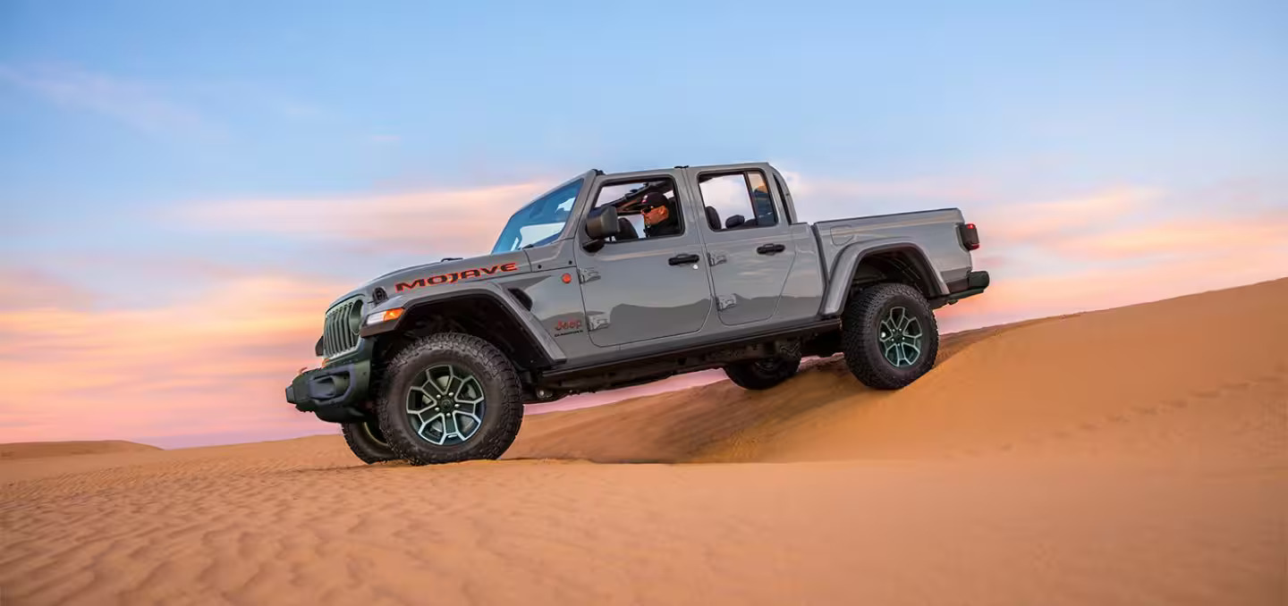 A gray jeep driving in the sand.