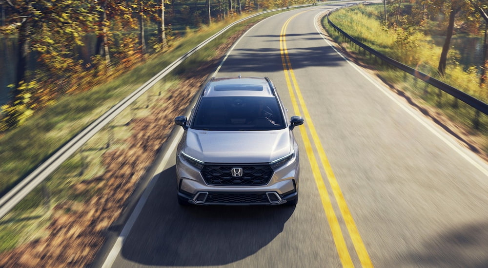 White 2026 Honda CR-V Sport Touring Hybrid driving down a road.