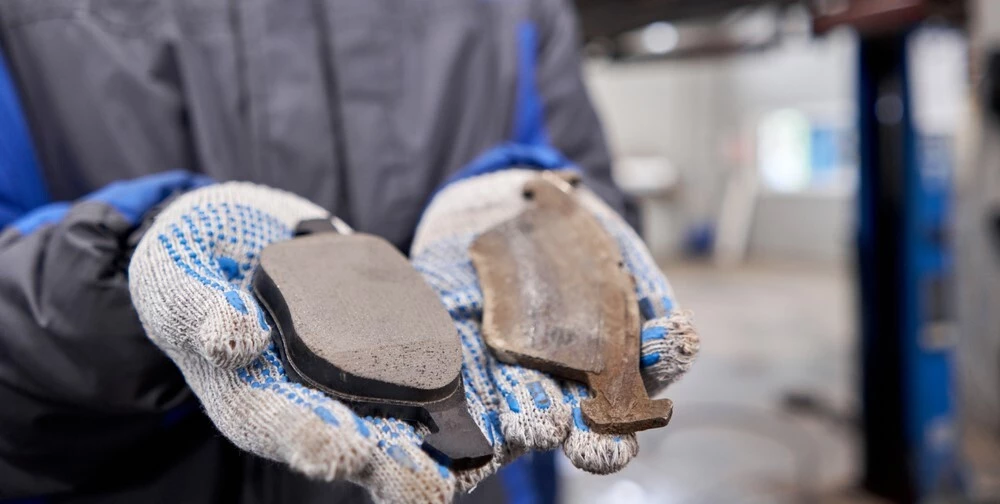 A person is offset into background, his hands are im frame, gloved, and holding two more burnt out brake pads