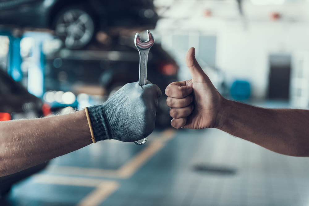 Close-up Thumb Up and Mechanics Hand with Tool. Automobile Master Wearing Gloves Showing Positive Gesture after Finishing Work. 