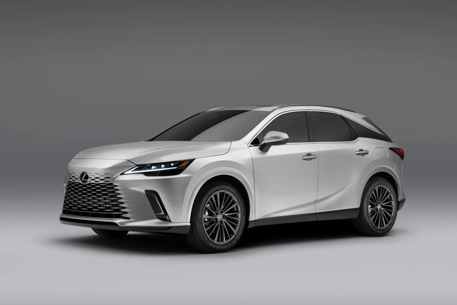 A white Lexus SUV photographed at a front three-quarter angle in a studio setting, showing its spindle grille and sharp LED headlight design.