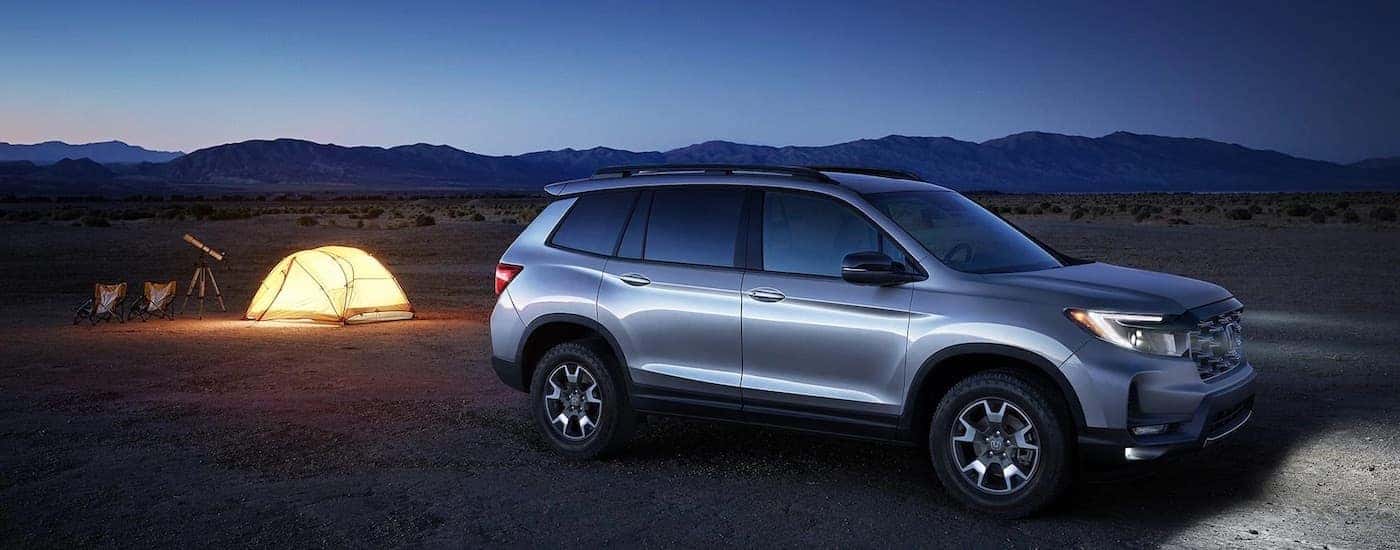 A silver 2023 Honda Passport is shown parked off-road near some tents.
