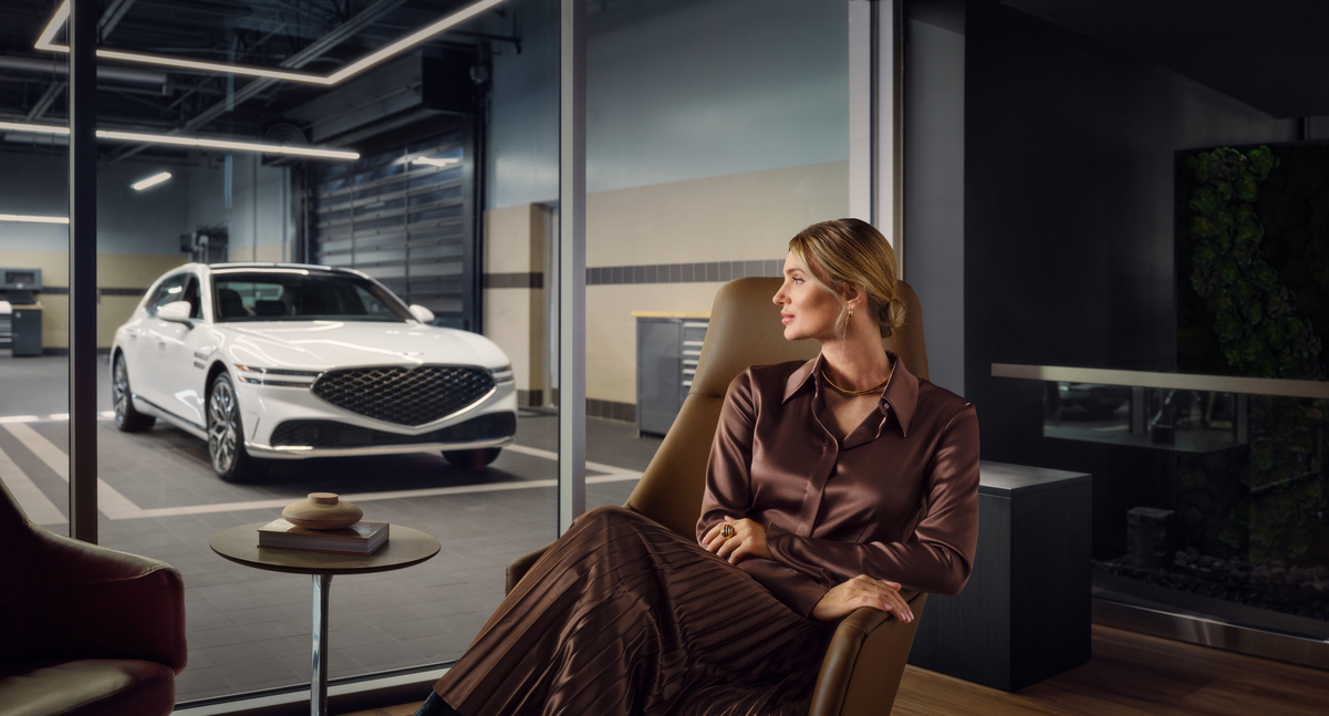 View of Genesis G90 in service center through glass, person seated in waiting area.