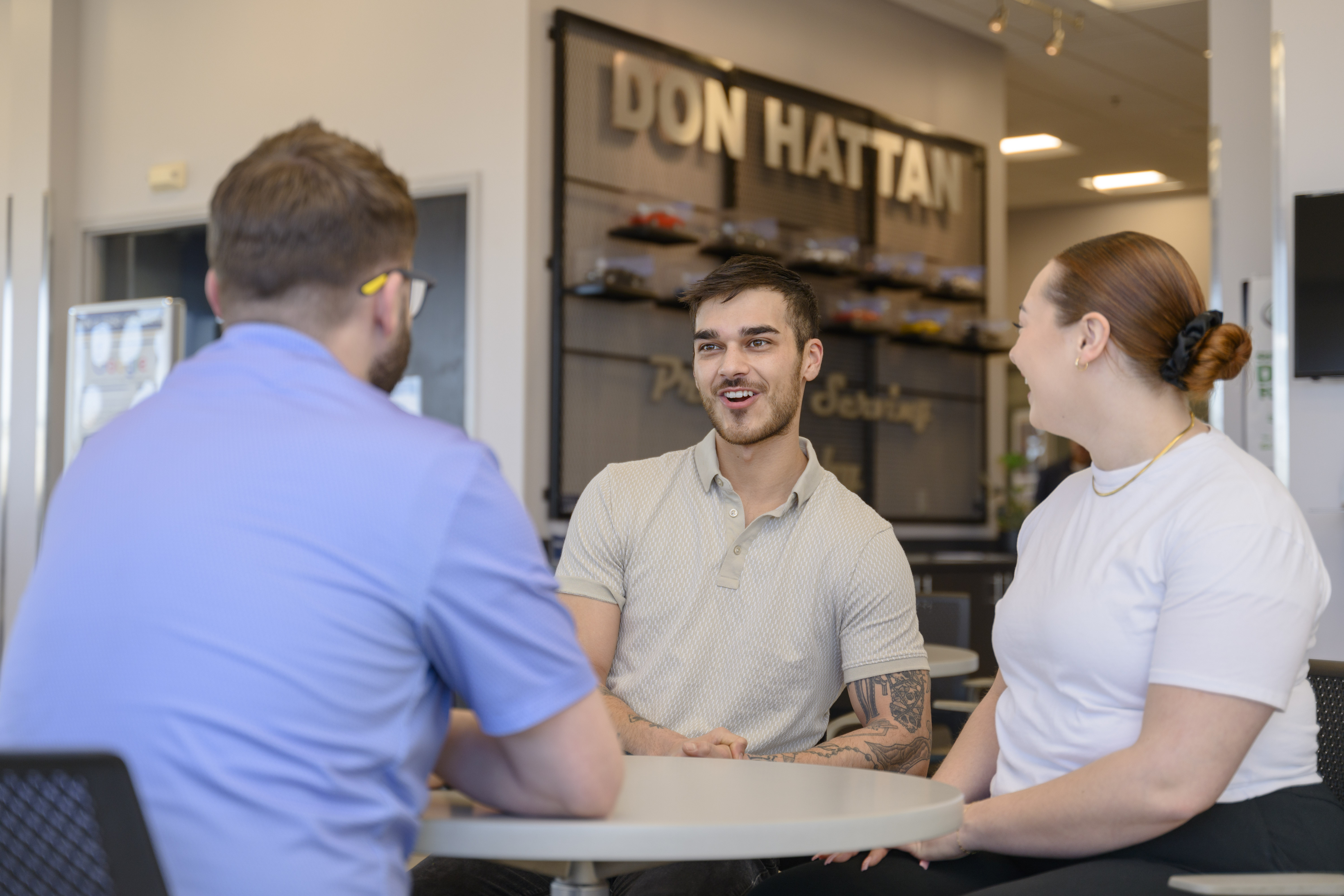 A man and woman sitting at a table with a salesperson from Don Hattan Derby auto dealership reading a vehicle history report