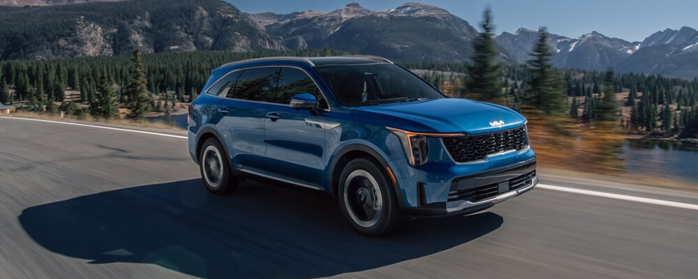 2025 Kia Sorento Hybrid driving on scenic road with mountains and trees in background, showcasing its family-friendly design and hybrid efficiency.