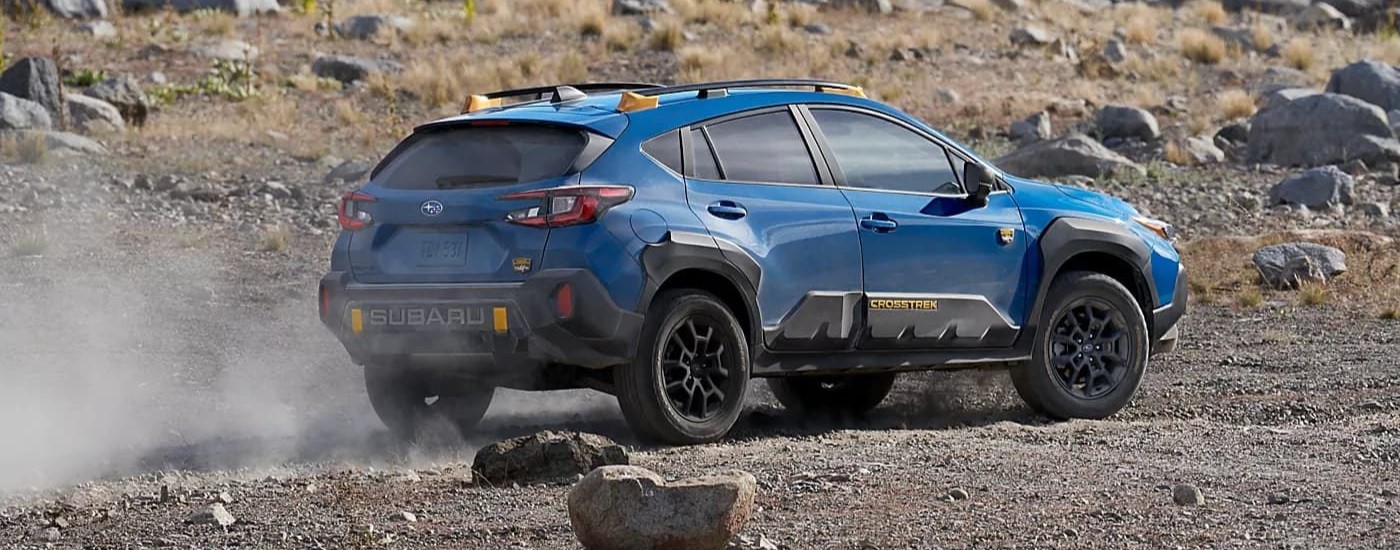 A blue 2024 Subaru Crosstrek Wilderness driving on gravel.