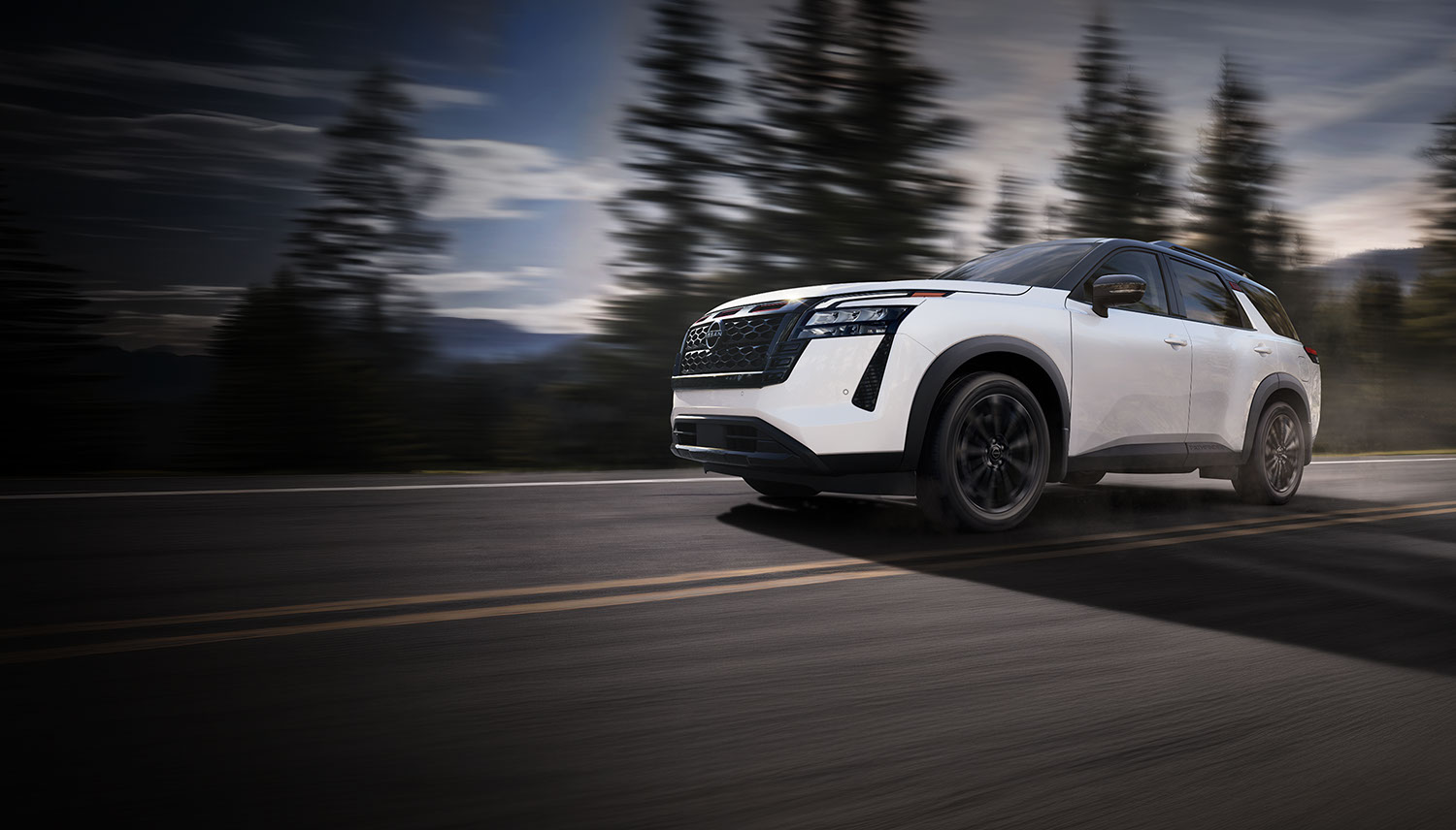 2027 Nissan Pathfinder in white driving along a mountain road lined with pine trees