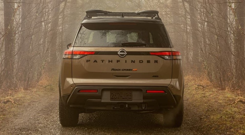 Rear of a brown 2025 Nissan Pathfinder Rock Creek driving down a forest path