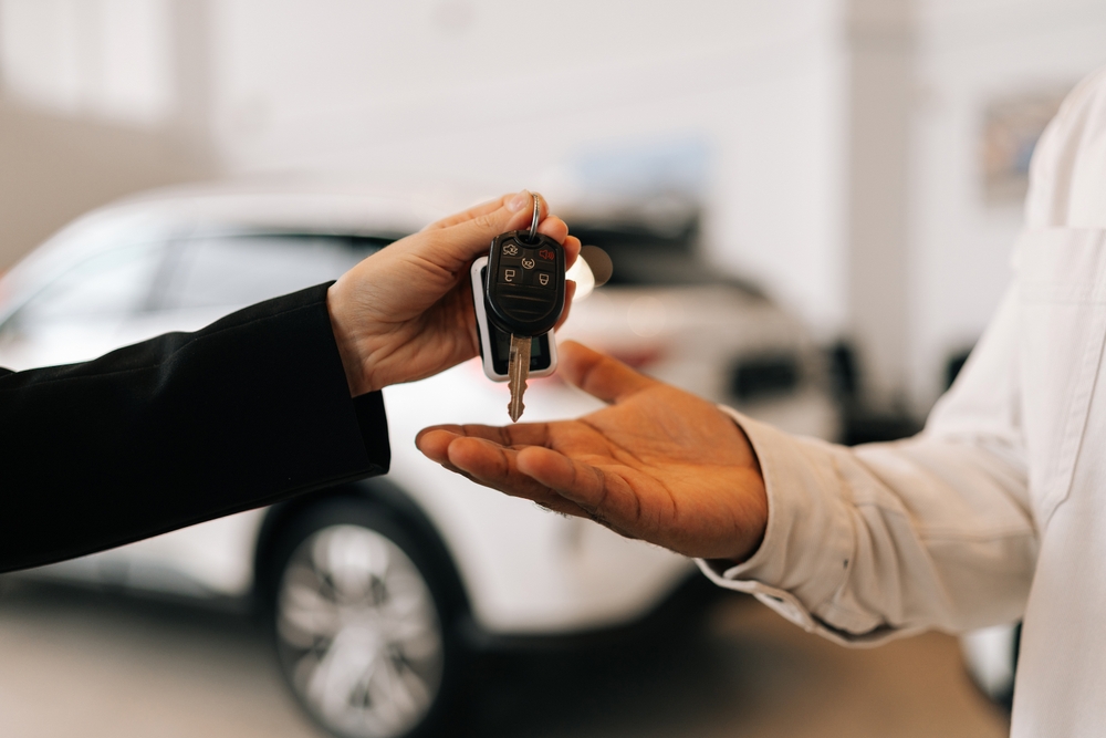 Closeup hand of unrecognizable black male buyer getting car key and greetings from auto dealer while buying new auto in dealership. African American car owner during handing over keys at auto showroom