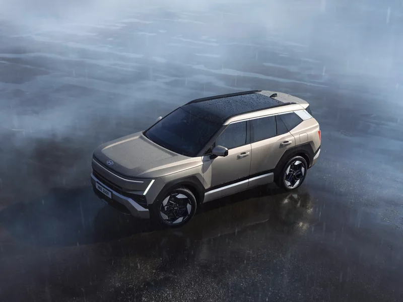 Warm gray 2027 Hyundai Tucson SUV with a black roof seen from above on a wet, reflective surface in rain and mist