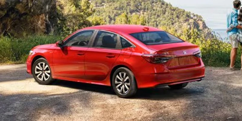 A red Honda Civic sedan parked on a sunny, wooded dirt path