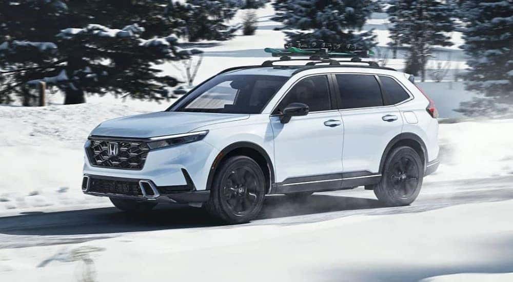 A white 2023 Honda CR-V Sport Touring Hybrid is shown on a snowy path after leaving a Honda dealer near Clarence.