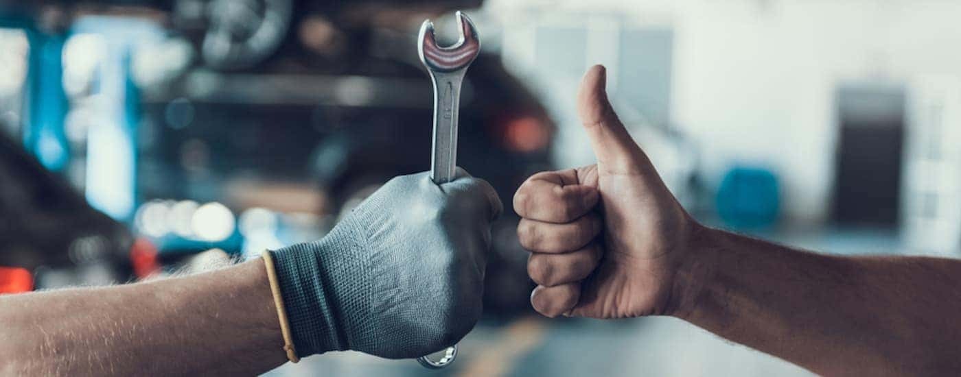 A hand offering a thumbs up to a gloved hand holding a wrench.