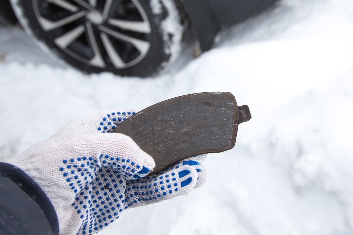 Hand Holding Brake Pad near Vehicle in the Snow