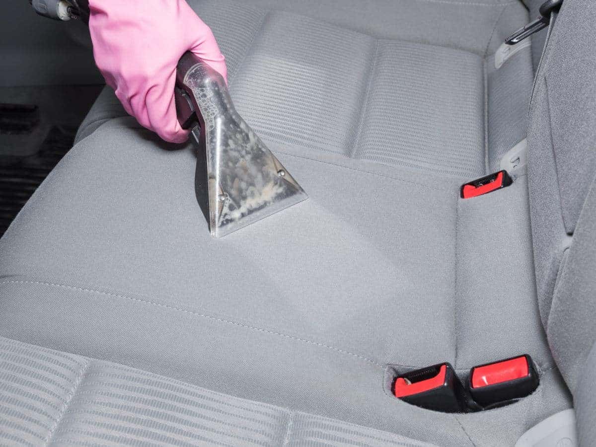 Gloved hand steam cleaning a cloth car seat