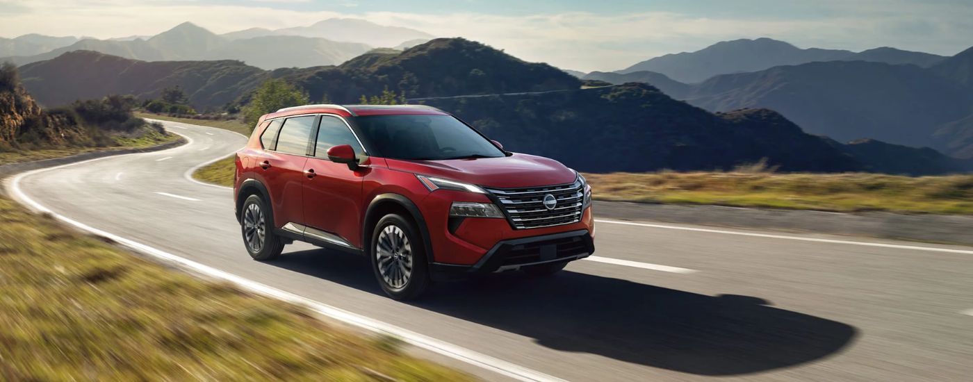 Red 2026 Nissan Rogue driving on flat, paved road.