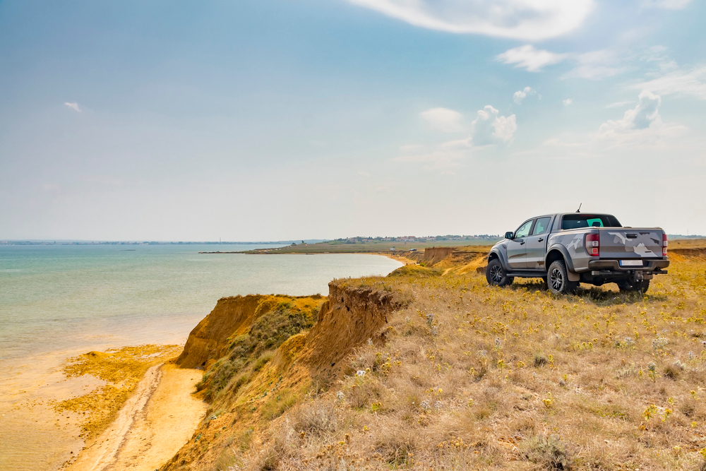 truck parked on the cliff of a shoreline, looking out towards the water