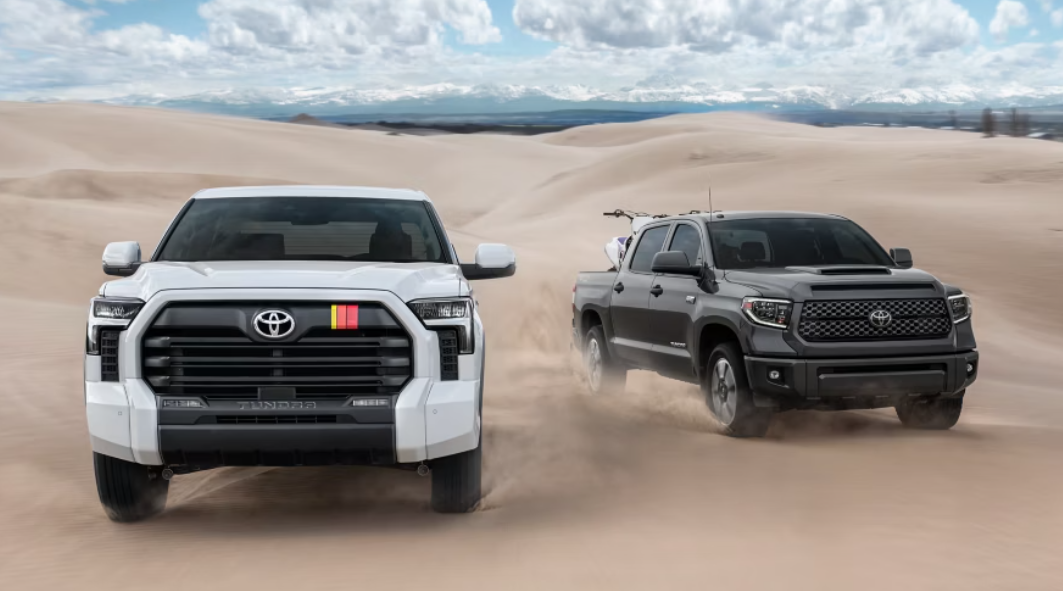 Two new 2025 Toyota Tundra trucks, one in black paint and one in white paint, offroading in sand.