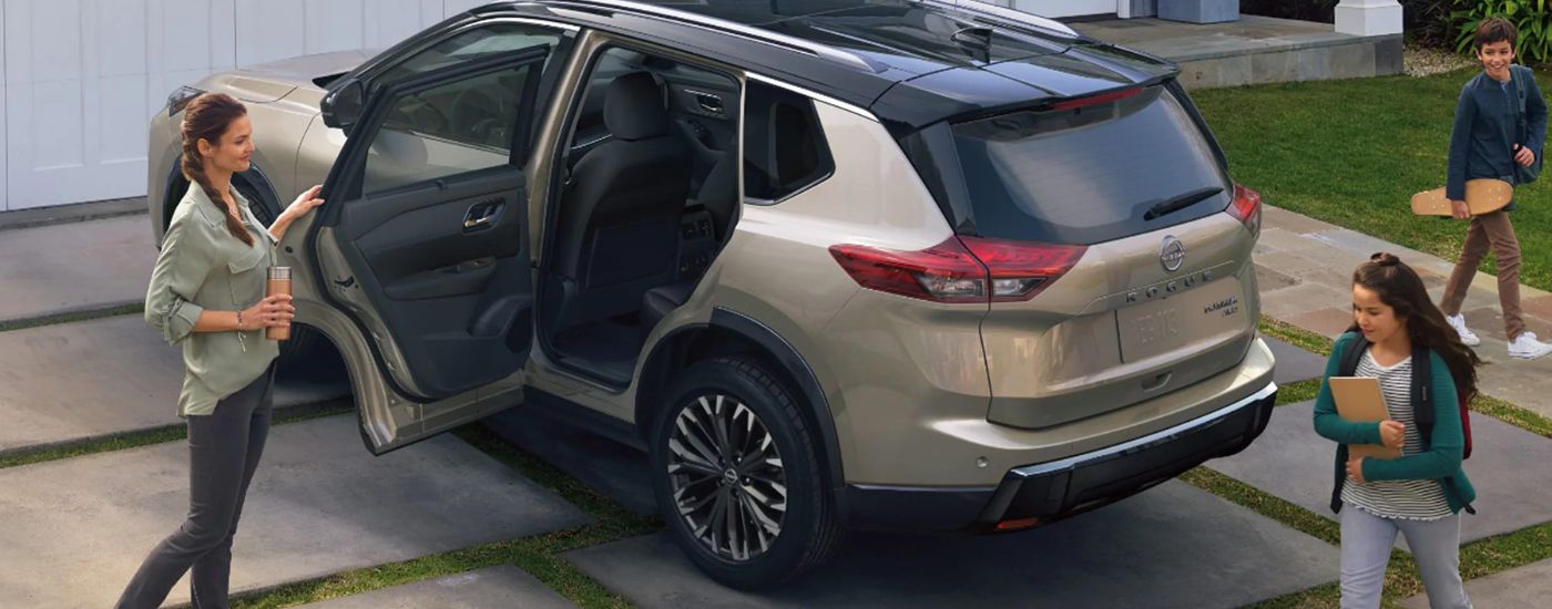 Tan 2026 Nissan Rogue in a driveway with a mother holding a rear door open for her kids.