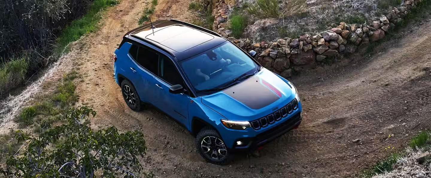 A blue Jeep Compass driving on a dirt road.