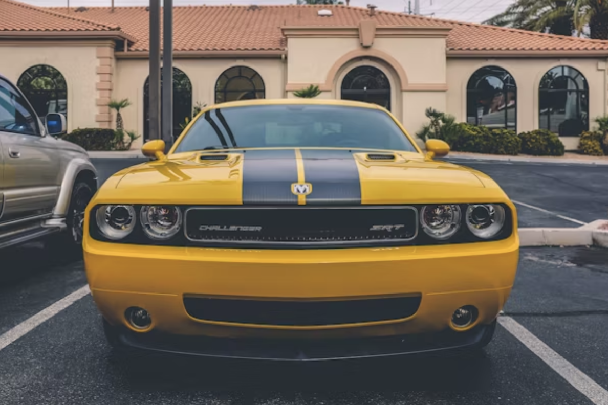 Front view of a bright yellow Dodge Challenger SRT with a black stripe, parked outside a building.