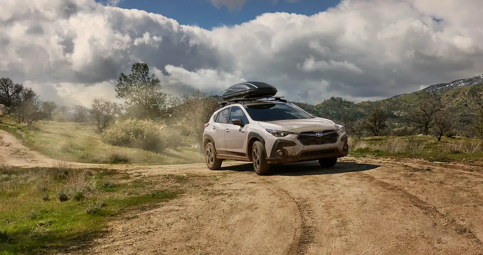 Tan Subaru Crosstrek with a roof box on a dirt road