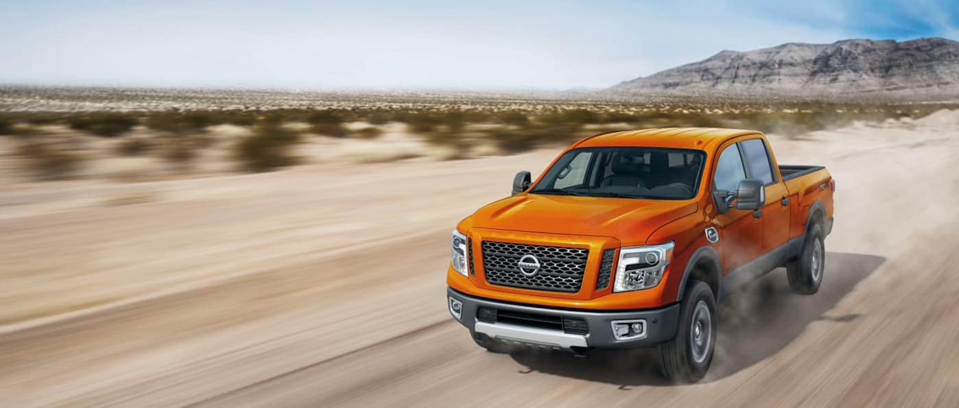 an orange nissan pick up driving through a southwest desert