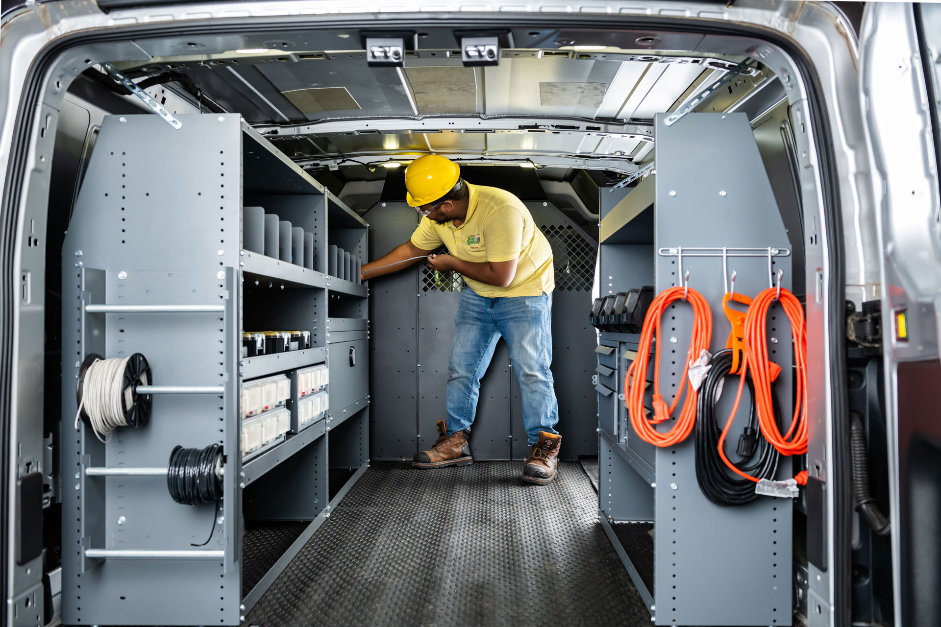 An electrician gets a wire off a spool inside a Sprinter van upfitted with shelving for wires and electrical items