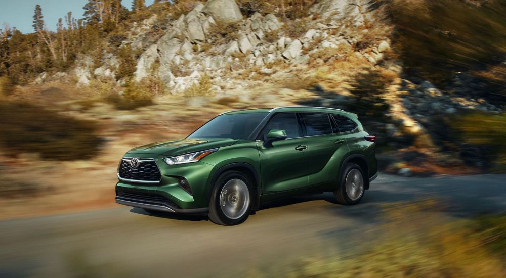 Green 2023 Toyota Highlander, a used car for sale, driving past cliffs.