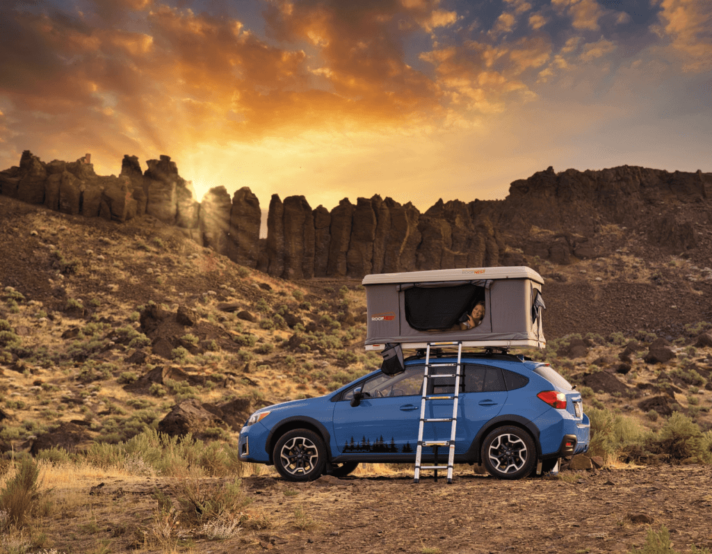 Blue Subaru Crosstrek with a rooftop tent in the desert at sunset