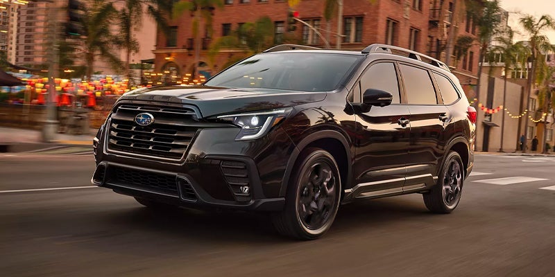 Black Subaru Ascent Onyx Edition driving down a palm-lined city street at dusk