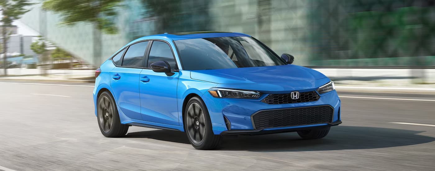 A blue 2024 Honda Civic Hatchback Sport Touring driving on a winding highway.