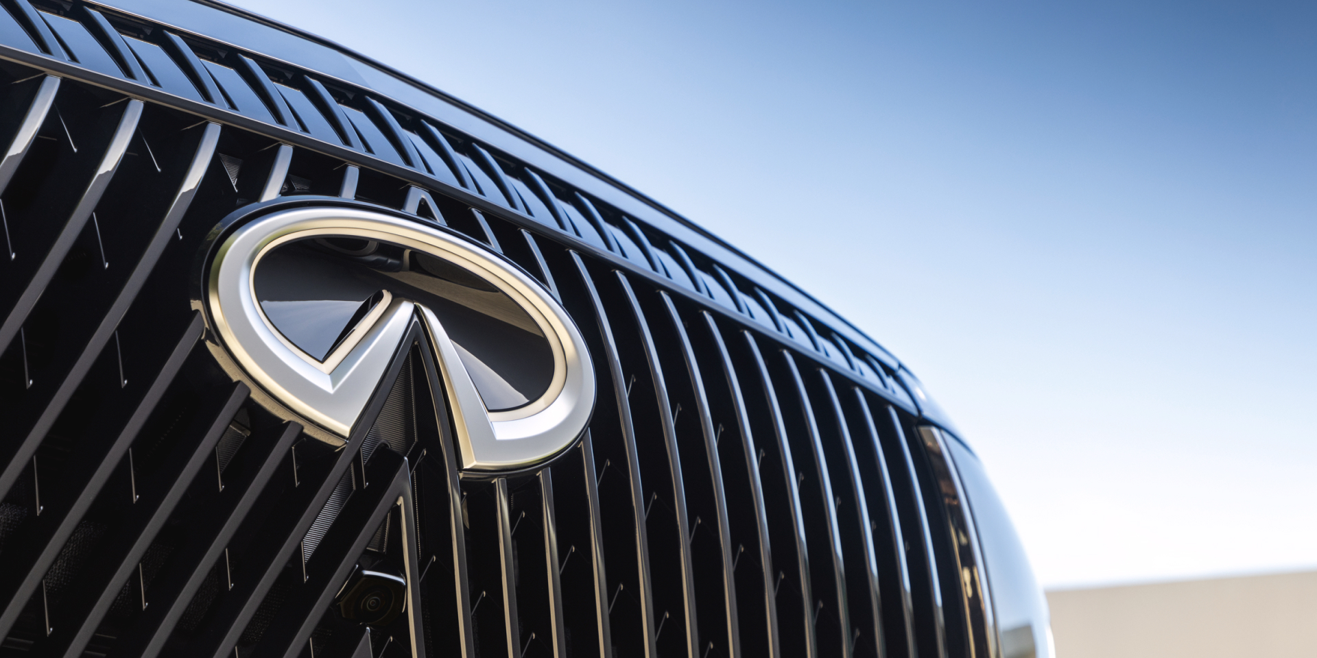 Close-up of the chrome INFINITI emblem and vertically slatted grille on the 2027 INFINITI QX80 with an integrated front camera.