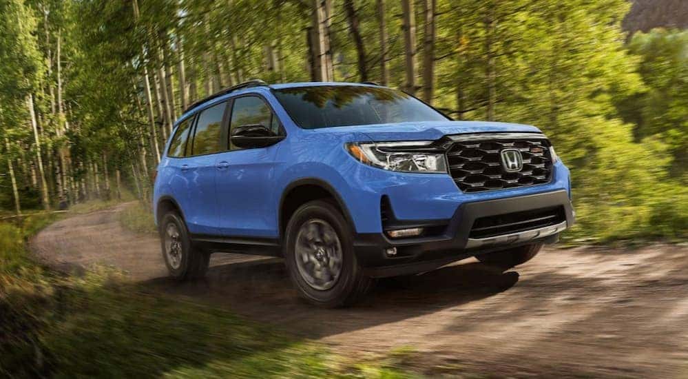 A blue 2024 Honda Passport Trailsport driving on a dirt path off-road.