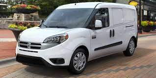 A Ram Promaster City parked on the side of the road in the city with some greenery in the background