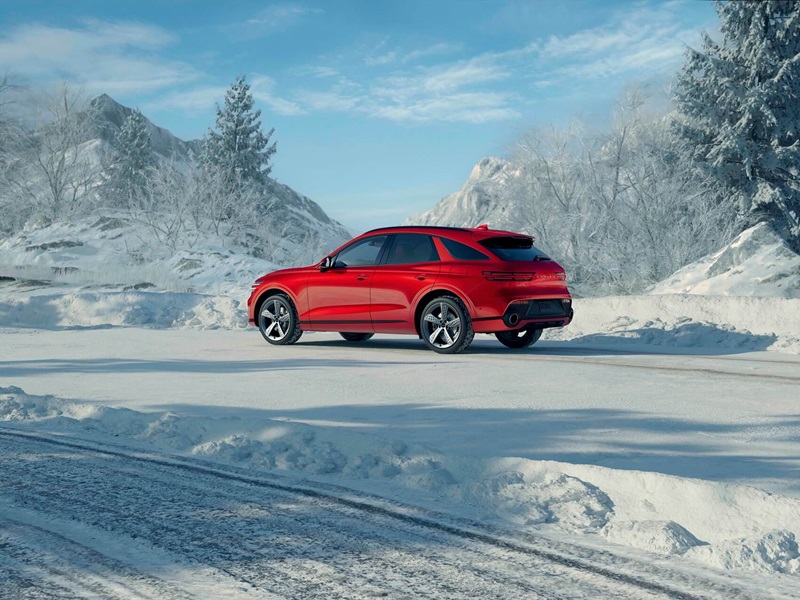 Red Genesis GV80 Coupe parked on a snowy mountain road surrounded by frosted pine trees.