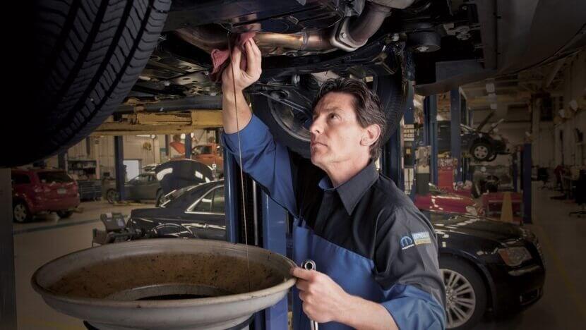Mopar technician checking the underside of a vehicle on a lift during an oil change