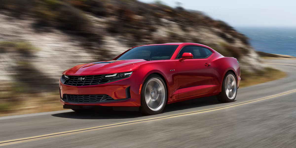 A red camaro driving on the road.