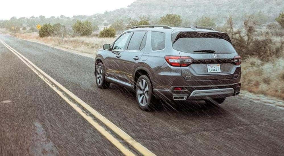 A gray 2023 Honda Pilot Elite is shown driving on a highway in the rain.