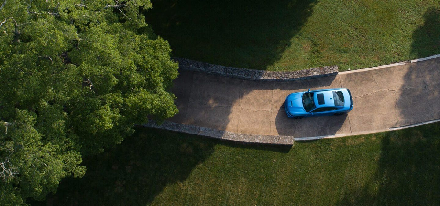 Blue SUV driving along a winding road through green trees, seen from above