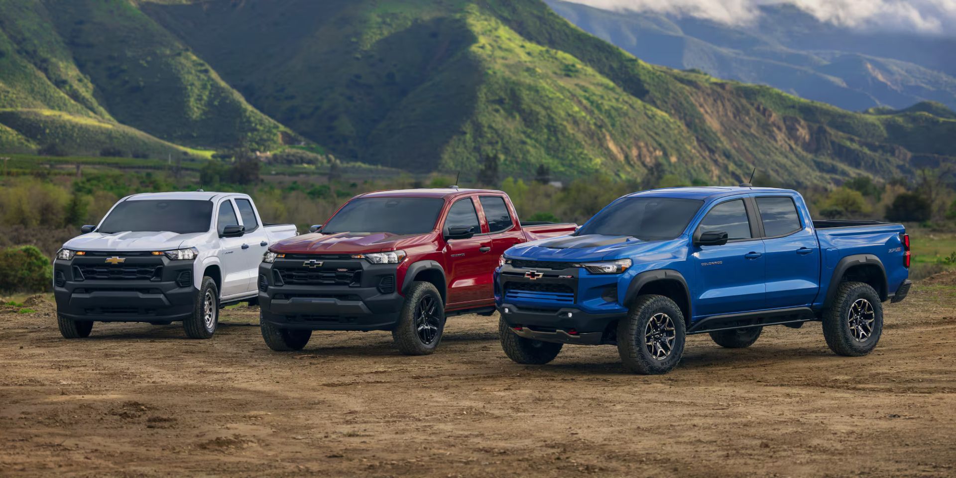lineup of a white, red and blue chevrolet colorado parked on dirt with mountains in the background