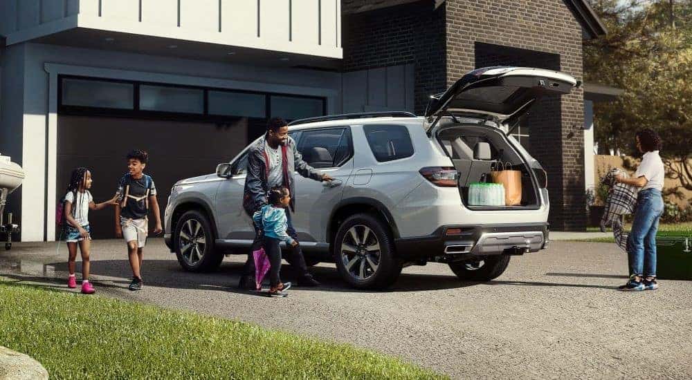 A white 2023 Honda Pilot is shown with a family on a driveway.