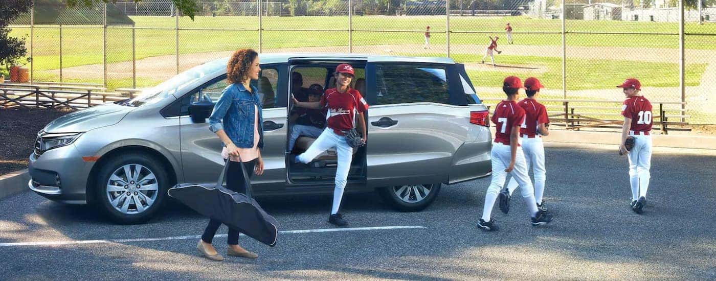 A silver 2021 Honda Odyssey is shown from the side with youth baseball players exiting the sliding doors.