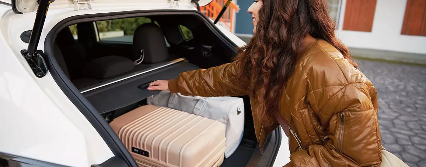 Woman putting luggage in the back of a white 2026 Subaru Impreza.