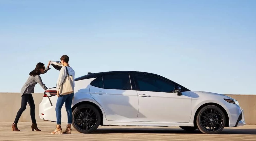 Two people inspecting the trunk of of a white 2022 Toyota Camry for sale