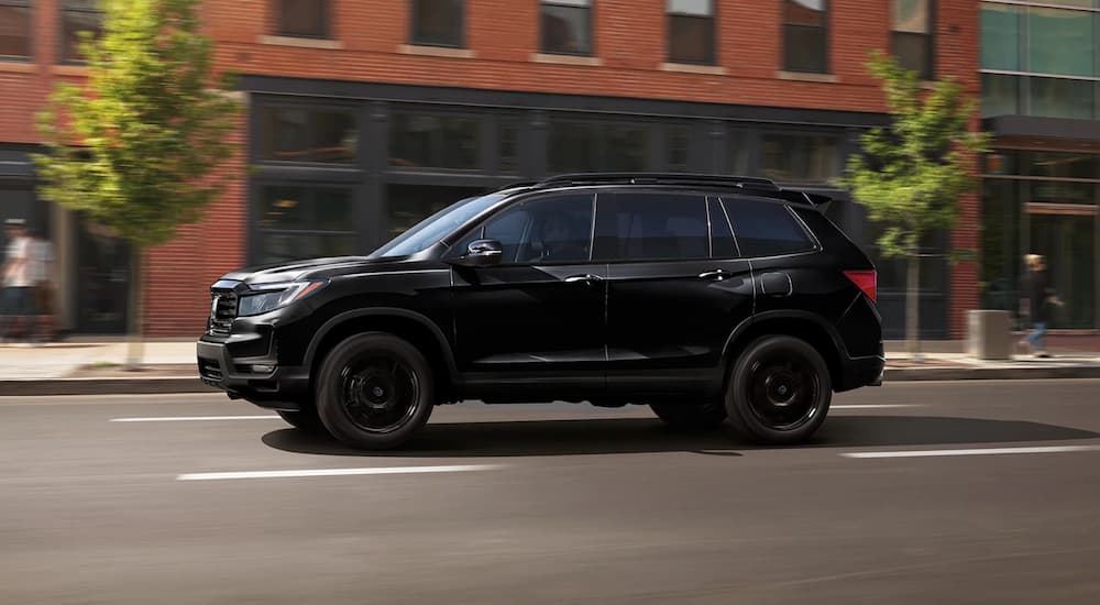 Side of a black 2026 Honda Passport Black Edition driving down a city street.