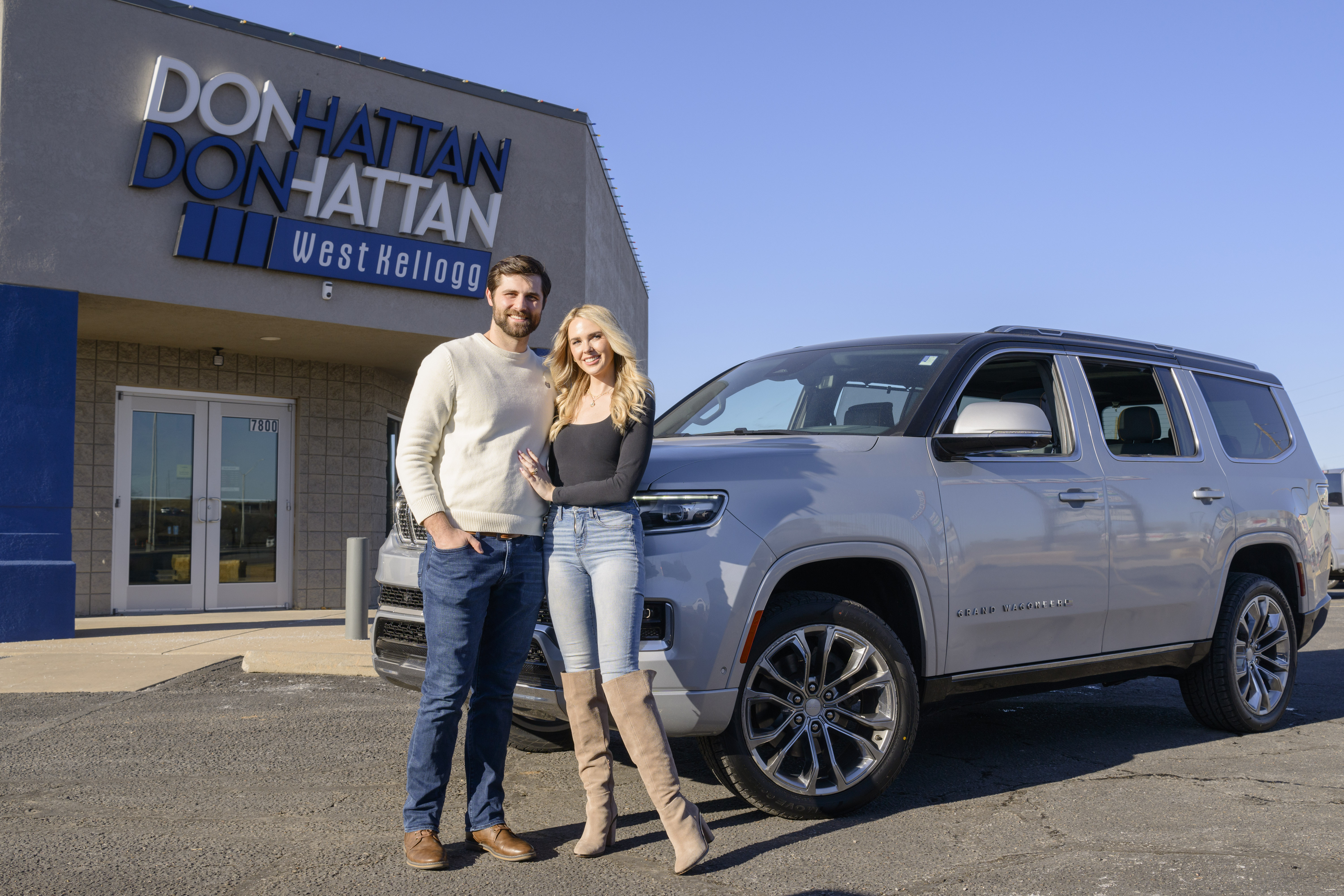 A man and woman standing next to a large silver SUV outside of Don Hattan Dealerships auto group in Wichita, KS